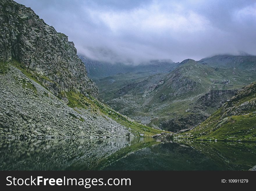 Gray and Green Mountains With Body of Water Under Cloudy Sky