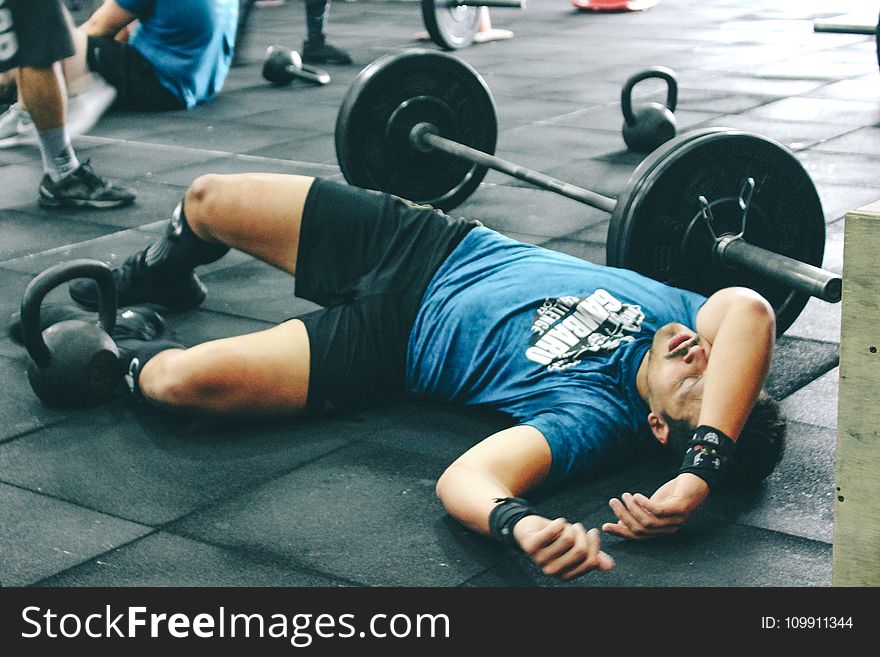 Man Lying on Rubber Mat Near Barbell Inside the Gym