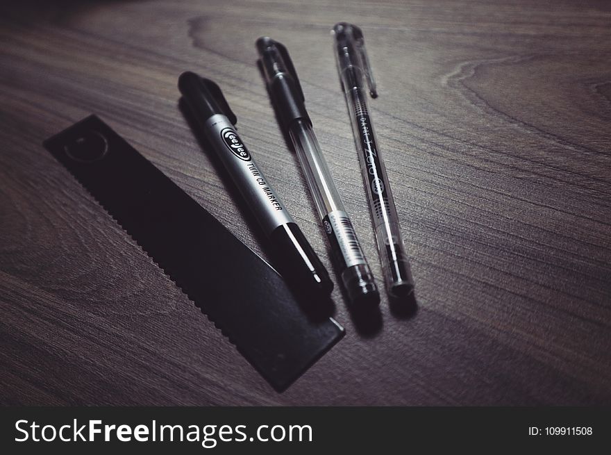 Three Ballpoint Pens and Black Ruler on Beige Wooden Surface