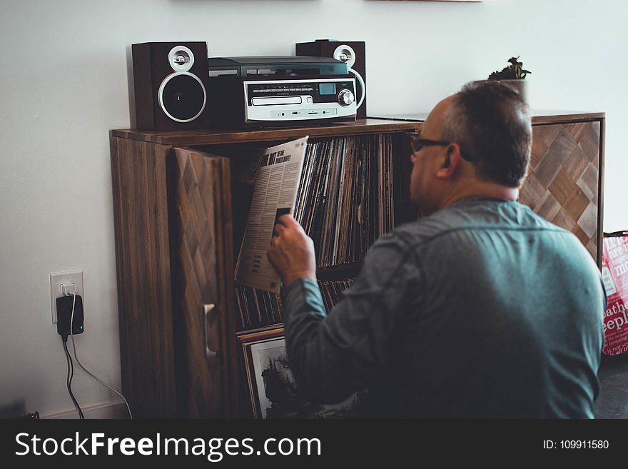 Man In Gray Longsleeve Shirt Holding Book In Front Of Brown Wooden Book Case