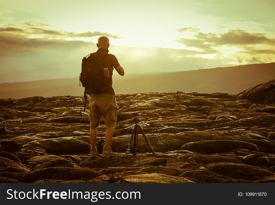 Man Beside Tripod on Rocks during Golden Hour