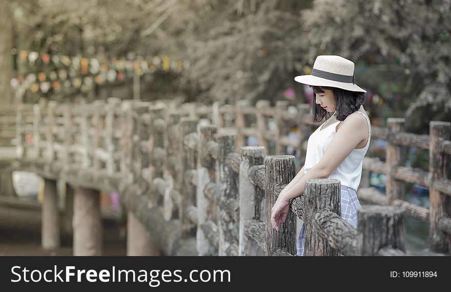 Woman Wearing White Tank Top and White Hat Standing on a Boardwalk
