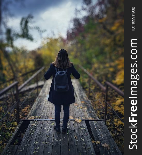 Selective Focus Photography of Woman Wearing Black Overcoat Standing on Wooden Bridge
