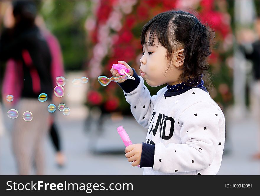 Toddler Girl Wearing White And Black Sweater Holding Plastic Bottle Of Bubbles At Daytime