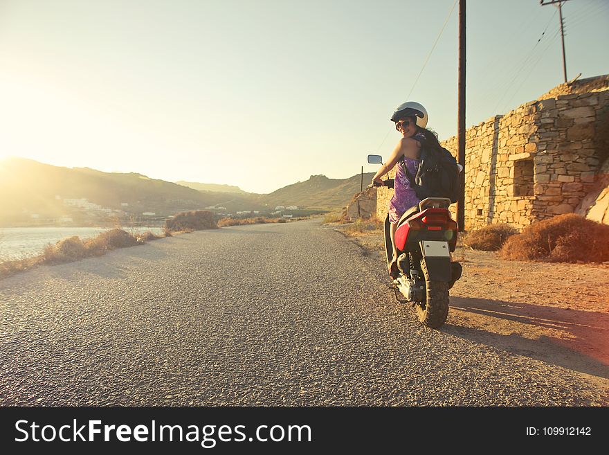 Woman Riding Motor Scooter Travelling On Asphalt Road During Sunrise