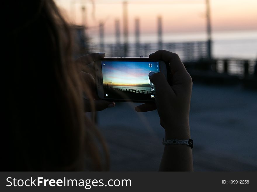 Brown Haired Woman Taking a Photo of Sunset