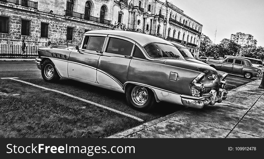 Greyscale Photo of Vintage Car Parked Beside Building