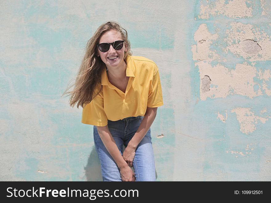 Woman Wearing Yellow Polo Shirt Standing in Front of Teal Concrete Wall