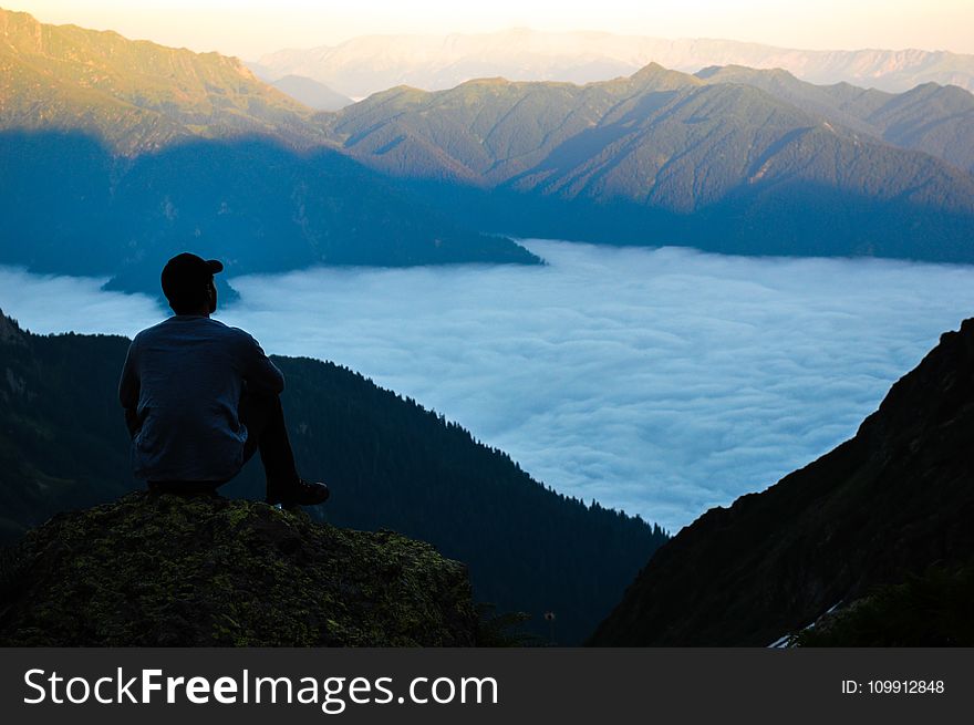 Man on the Edge of the Cliff Above the Cloudy Sky