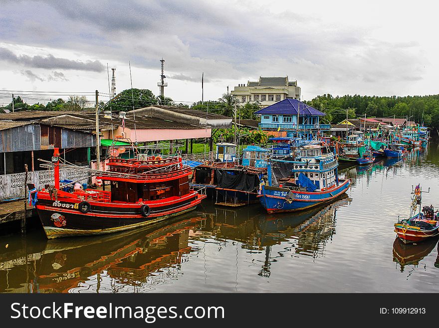 Assorted Color Boats on Body of Water Beside Houses and Trees Under White Sky at Daytime