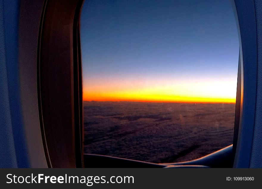 Photo of Airplane Window With View of Clouds and Golden Hour