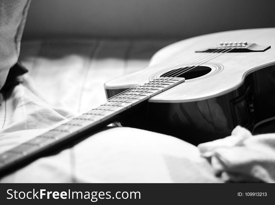 Gray Scale Photography of Acoustic Guitar on Bed