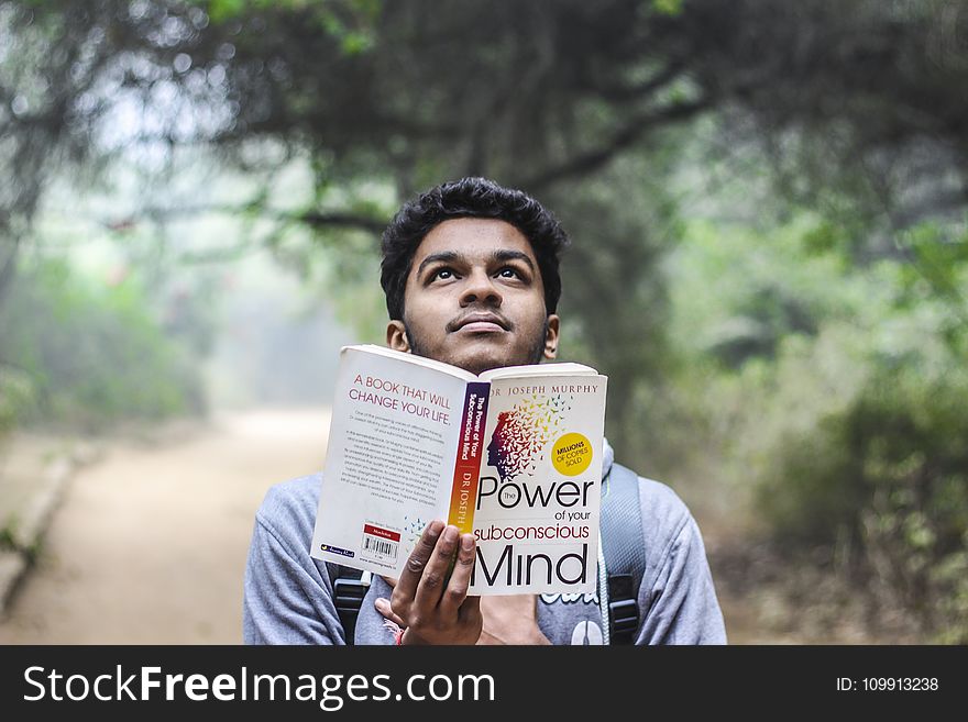 Man In Grey Shirt Holding Opened Book Looking Upward