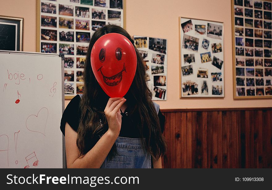 Woman Holding Red Balloon on Her Face Photo Inside Classroom