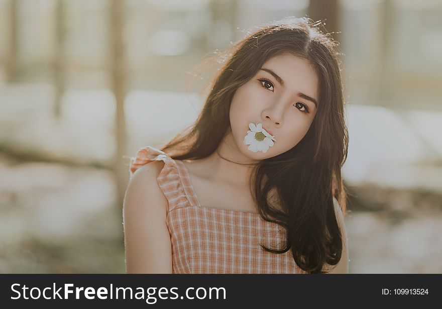 Woman Wearing Orange Sleeveless Dress Bites White Petaled Flower