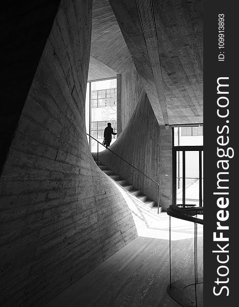 Person Standing Near Window Inside Building Near Stairs Grayscale Photo