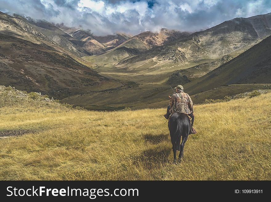 Man Riding Horse on Grass Near Mountains