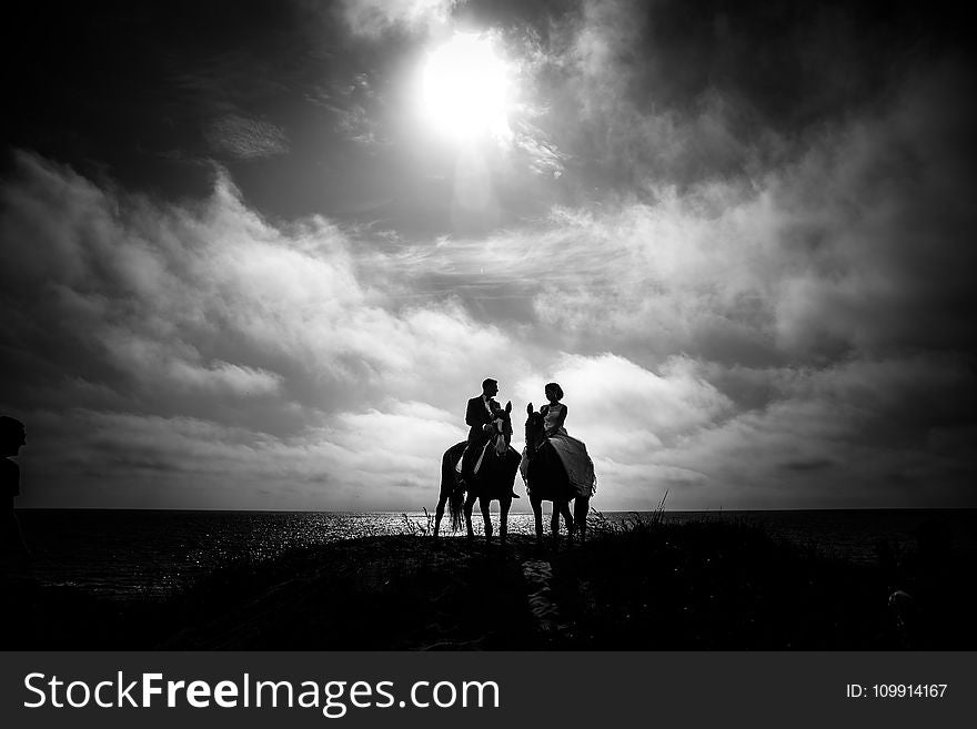 Grayscale Photography of Couple Riding on Horse With Body of Water and Sky As Background