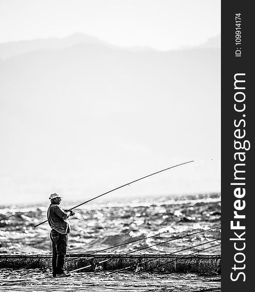 Man Standing Near Seashore Holding Fishing Rod on Grayscale Photography