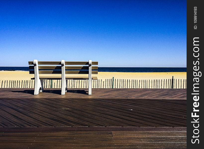 Brown-and-white Wooden Bench Facing Body Of Water Under Clear Blue Sky