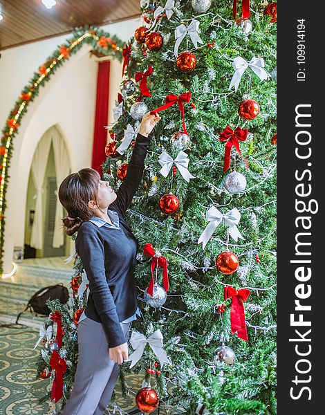 Woman Putting Ribbon Bow on Christmas Tree
