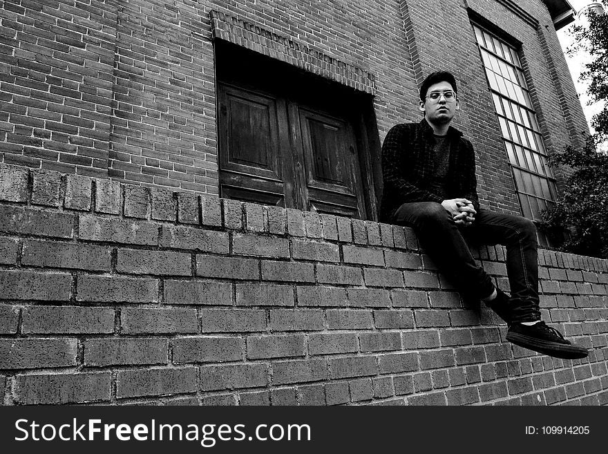 Grayscale Photography of Man Sitting on Brick Fence