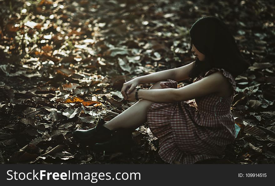 Photo of a Woman Sitting on the Ground Covered with Dried Leaves
