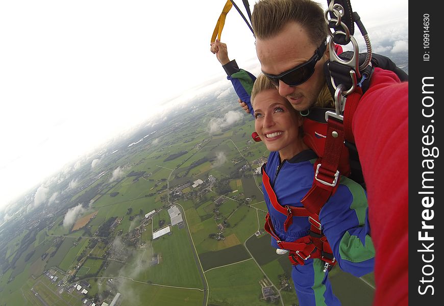 Couple Wears Red And Blue Long-sleeved Overalls And Body Harness With Parachute On Mid-air