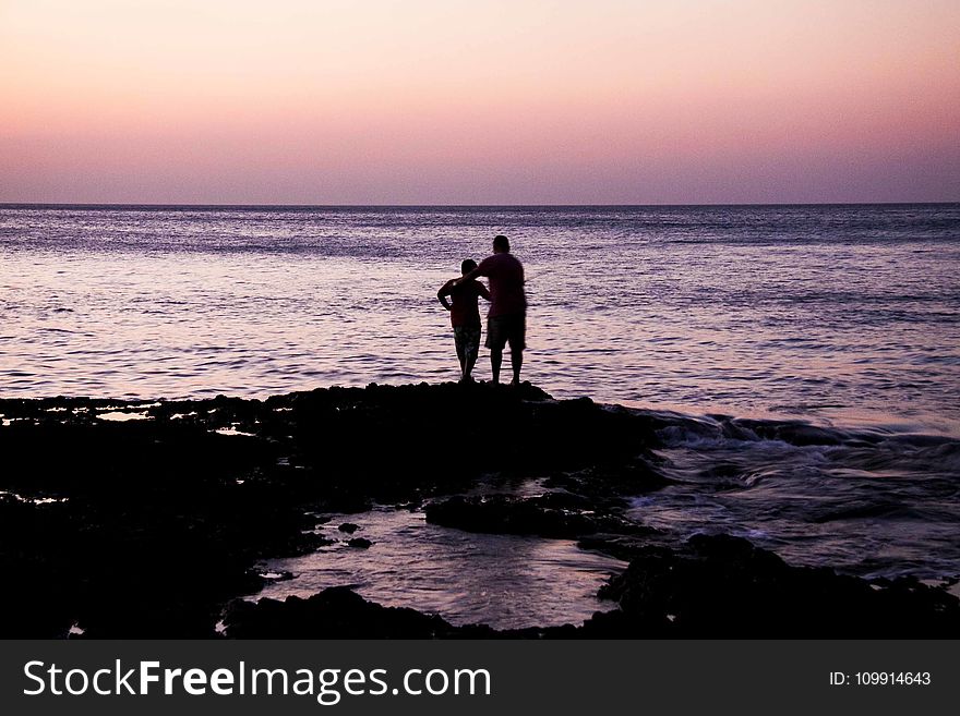 Father and Child Near on Body of Water during Sunset