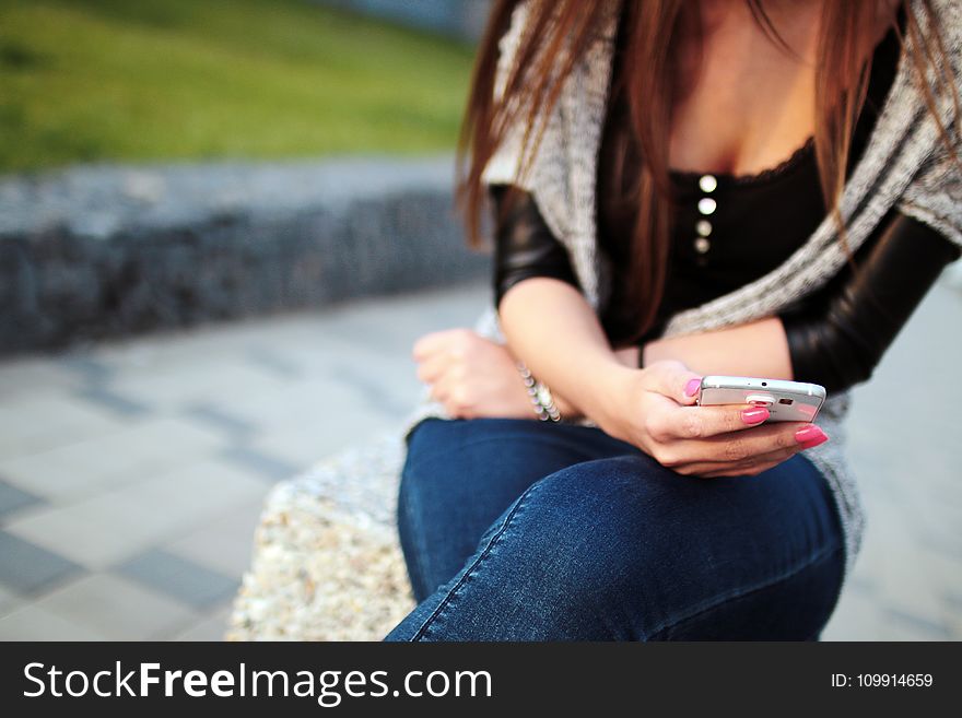 Woman in Black Elbow Sleeve Shirt and Blue Denim Jeans Sitting on the Grey Rock during Daytime
