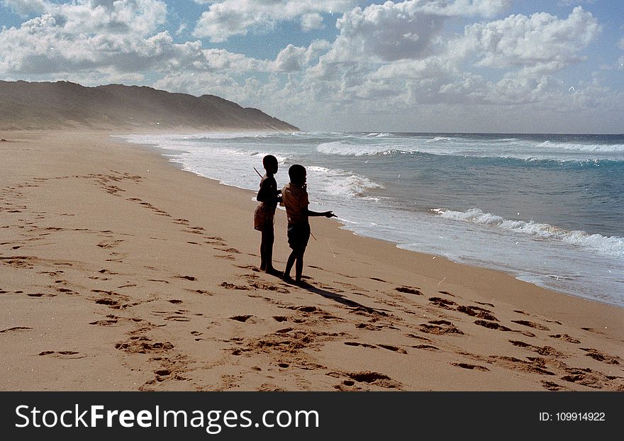 Two Children Stands on Shore Near Ocean at Daytime