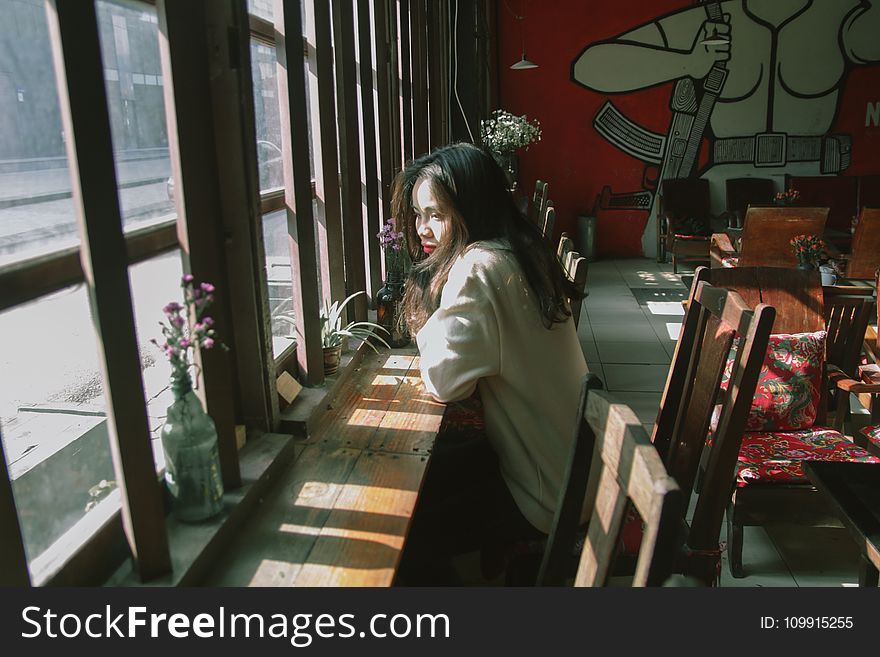 Woman Sitting on Chair Leaning on Table and on Facing Window