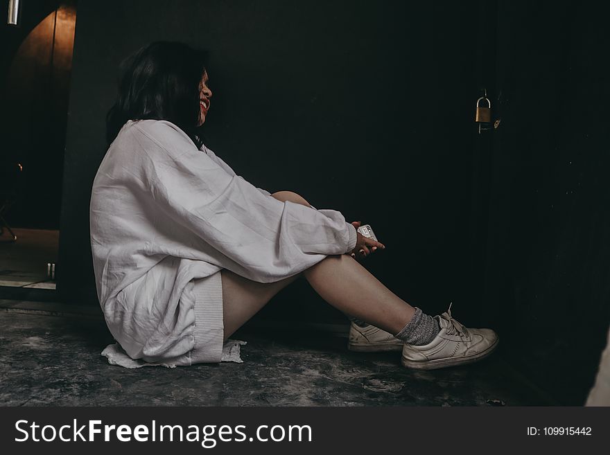 Woman Wearing White Dress Shirt And White Shoes Sitting On Black Flooring