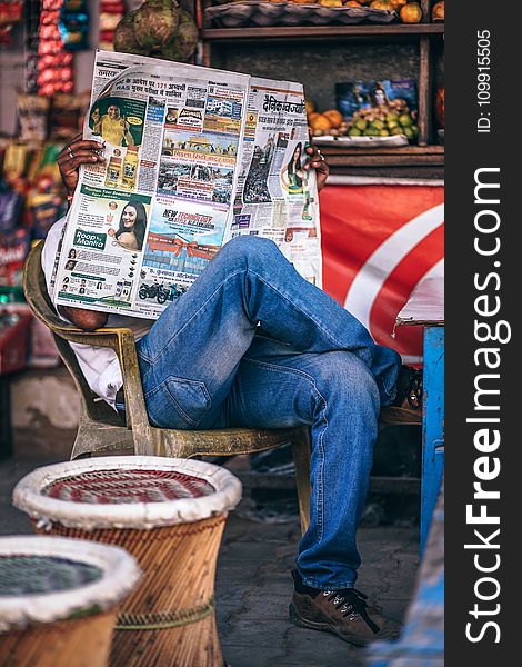 Man Sitting on Plastic Armchair Reading Newspaper