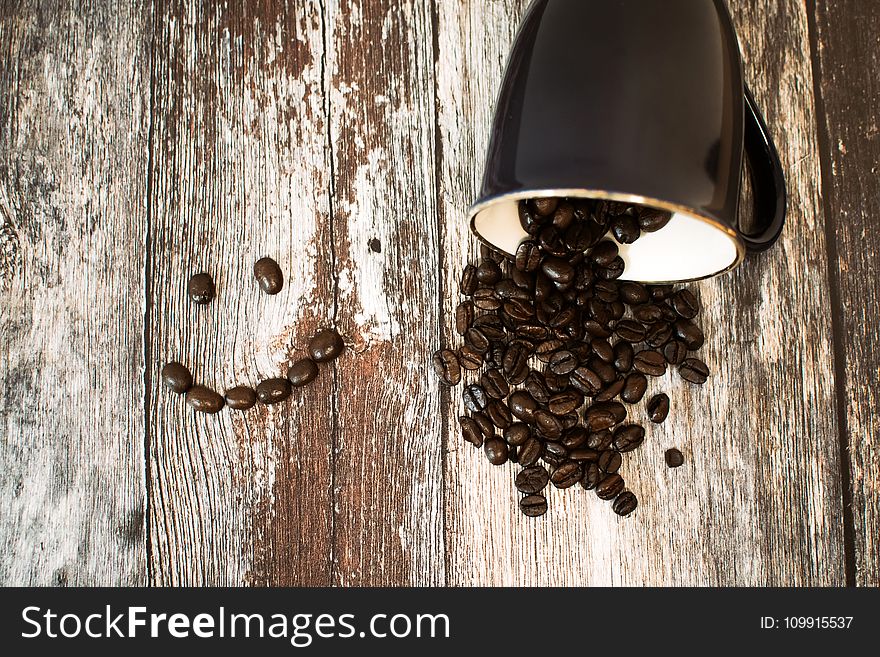Black Ceramic Cup With Coffee Beans All on Brown Wooden Surface