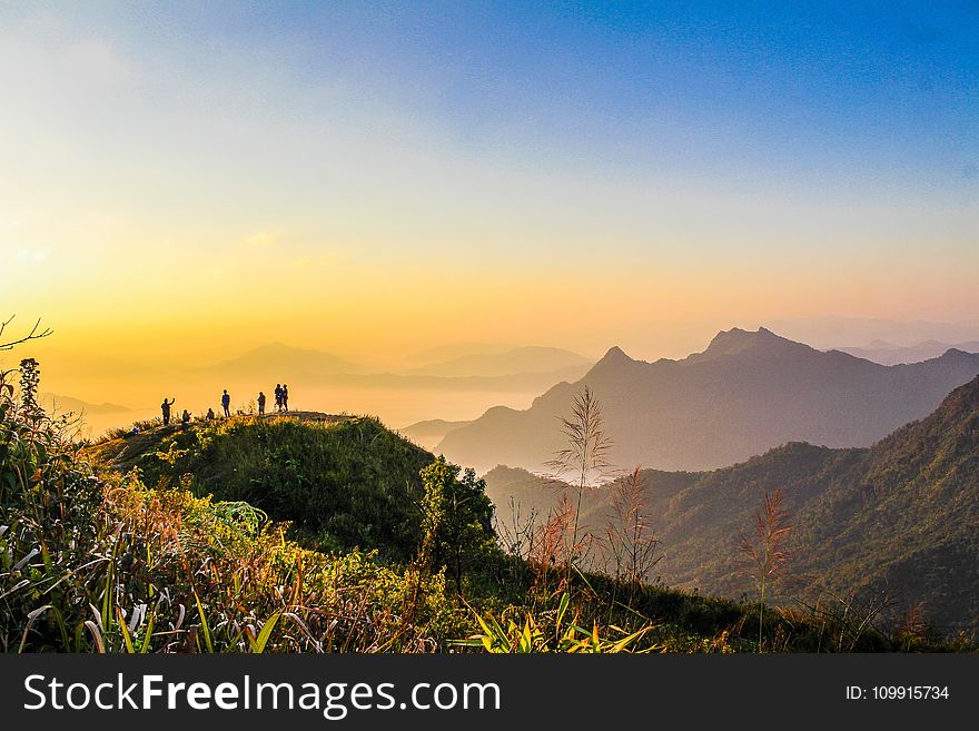 Photo of People Standing on Top of Mountain Near Grasses Facing Mountains during Golden Hours