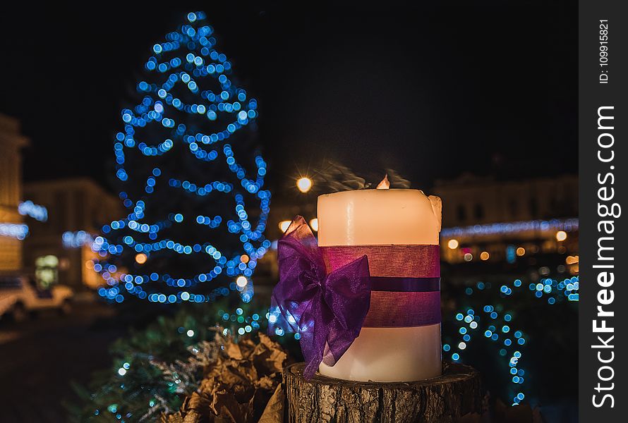 White Pillar Candle on the Log in a Distance of Blue Led Light Christmas Tree