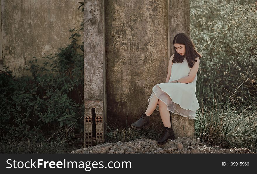 Woman Sitting on Slab Near Brown Wall