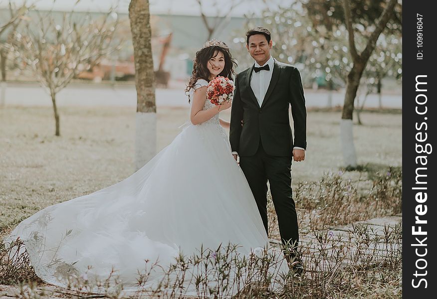 Woman Wearing White Wedding Ball Beside Man Wearing Black Notch-lapel Suit on Pathway Near the Green Grass Field