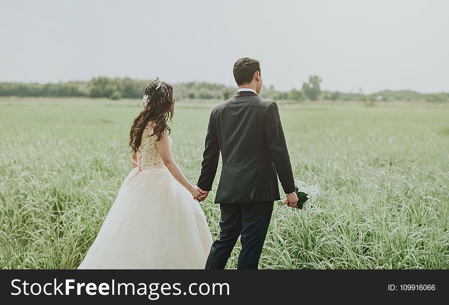Woman in White Wedding Dress Holding Hand to Man in Black Suit