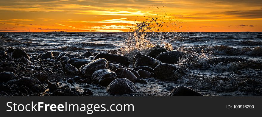 Waves Splashing At Stones On Beach During Sunset