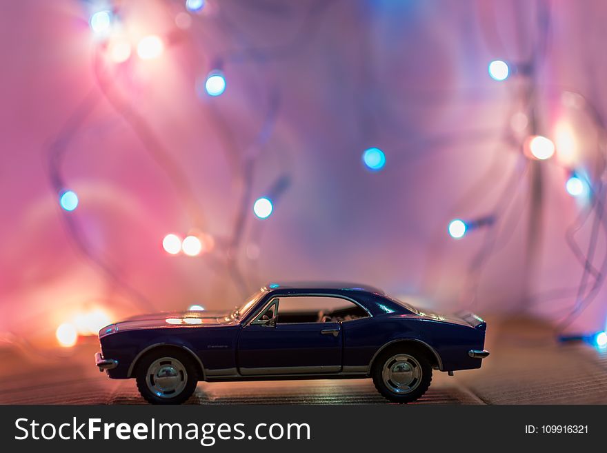 Selective Focus Photography Of Classic Blue Coupe Die-cast Model In Front Of String Lights On Table