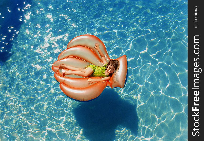 Girl Wearing Green Wet Suit Riding Inflatable Orange Life Buoy on Top of Body of Water