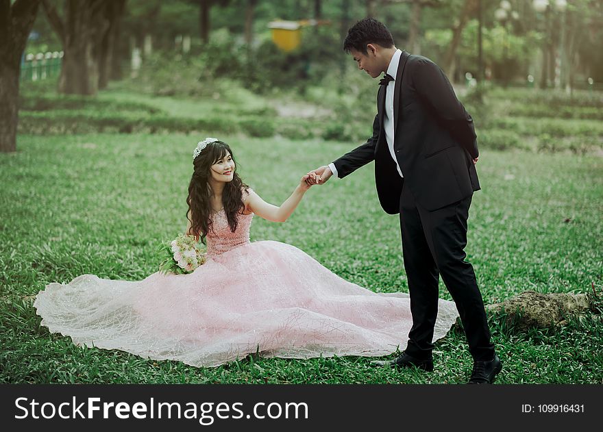 Man in 2-piece Suit Holding Woman in Peach-colored Wedding Gown White Holding Her Flower Bouquet