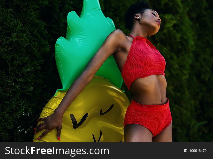 Woman Wearing Red Top and Bottoms Leaning on Yellow and Green Inflatable Standee
