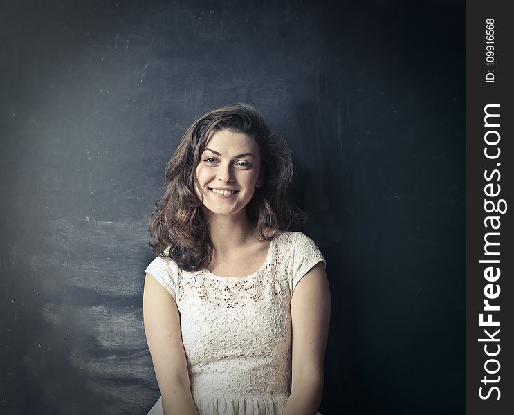 Brown Haired Girl In White Sleeveless Dress Standing Beside Black Painted Wall