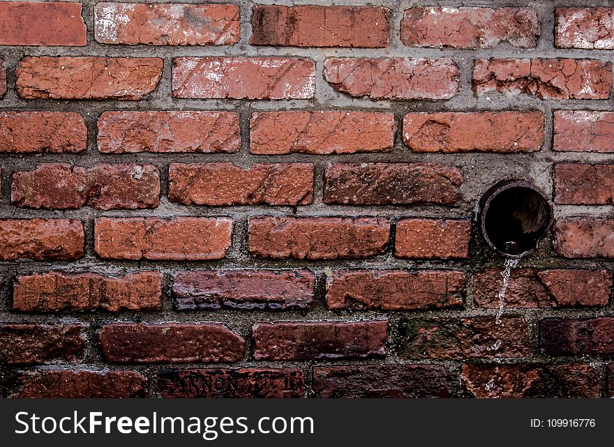 Round Brown Pipe Drainage With Liquid in Brown Bricked Concrete Wall