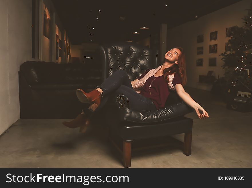 Woman In Maroon Scoop-neck Shirt Sitting On Black Leather Sofa Chair