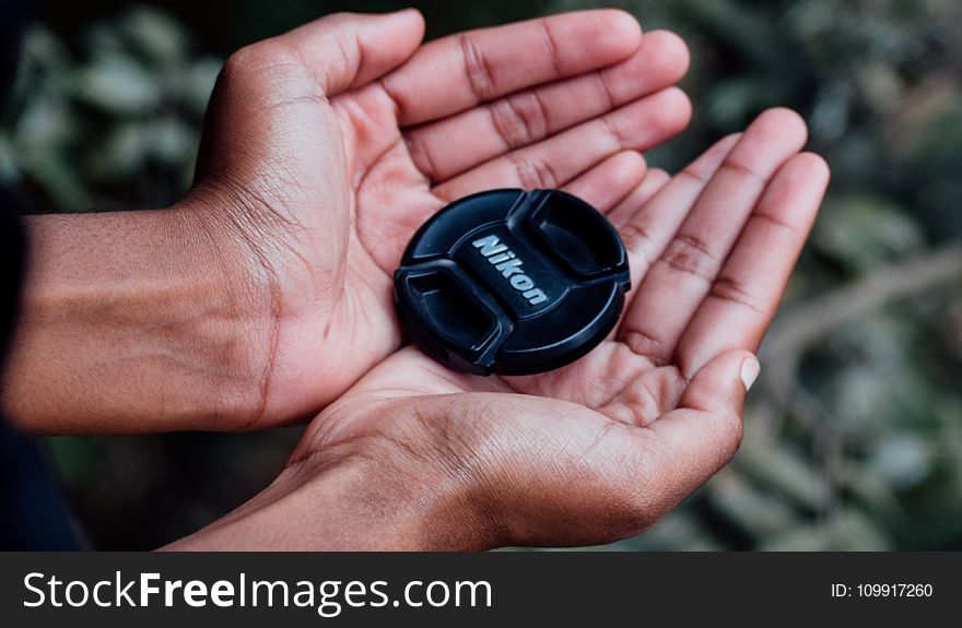 Black Nikon Camera Lens Cover on Left and Right Human Palms