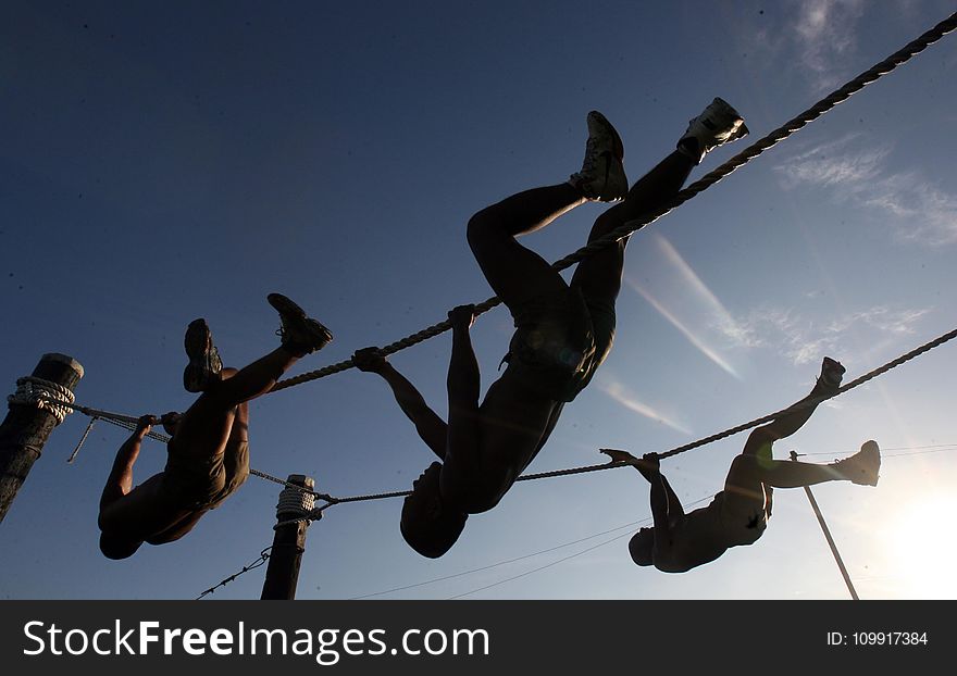 Three Man Climbing On Rope Under The Sunset